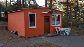 Une petite cabane orange avec une porte, deux fenêtres et une table entourée de chaises à l’extérieur.