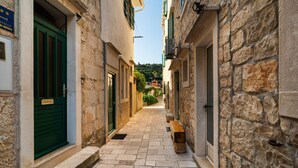 A narrow stone-paved alleyway between buildings with green shutters and a bench. - Cozy apartment in Povlja (Povlja)