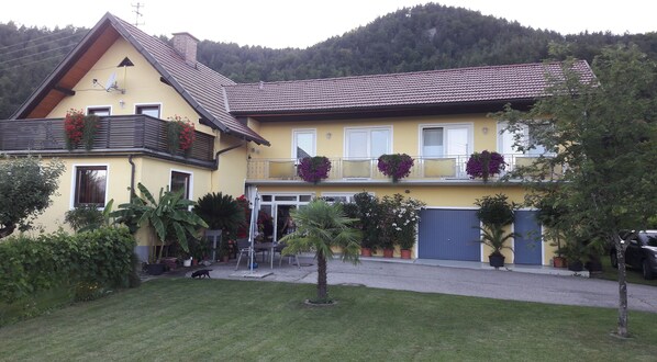 Ein gelbes, zweistöckiges Haus mit einem geneigten Dach, einem Balkon mit Blumenkörben und einer Garagentür.