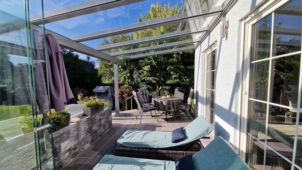 A glass-enclosed patio with lounge chairs, a small table, and potted plants. - Idyllic vacation apartment with pool, whirlpool and sauna near Leipzig (Eilenburg/ Ortsteil Behlitz)