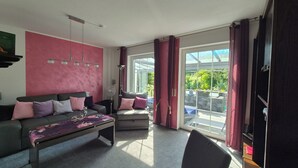 A living room with a sofa, armchair, and coffee table. There is a window with curtains, a fan, and a ceiling light fixture. - Idyllic vacation apartment with pool, whirlpool and sauna near Leipzig (Eilenburg/ Ortsteil Behlitz)