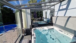 A glass-enclosed outdoor hot tub area with a pool and lounge chairs. - Idyllic vacation apartment with pool, whirlpool and sauna near Leipzig (Eilenburg/ Ortsteil Behlitz)
