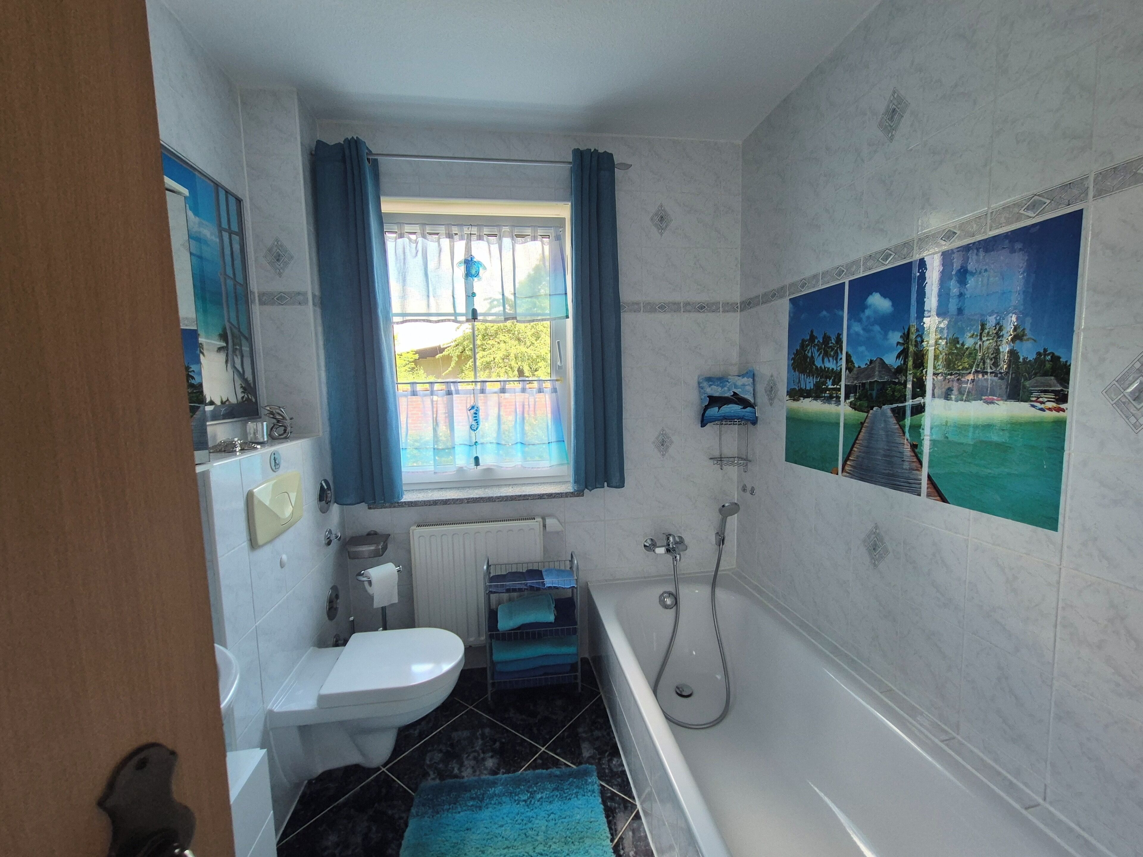 Ein Badezimmer mit Badewanne, Toilette, Waschbecken, einem Fenster mit Vorhängen und einer Dusche.