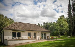 Ein eingeschossiges Haus mit einem Ziegeldach, einer überdachten Terrasse mit Gartenmöbeln und einem Rasen.