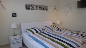 Ett sovrum med en säng, två sängbord, en lampa och väggdekorationer, inklusive orden ”OSTSEE” och ”SEA SIDE”.