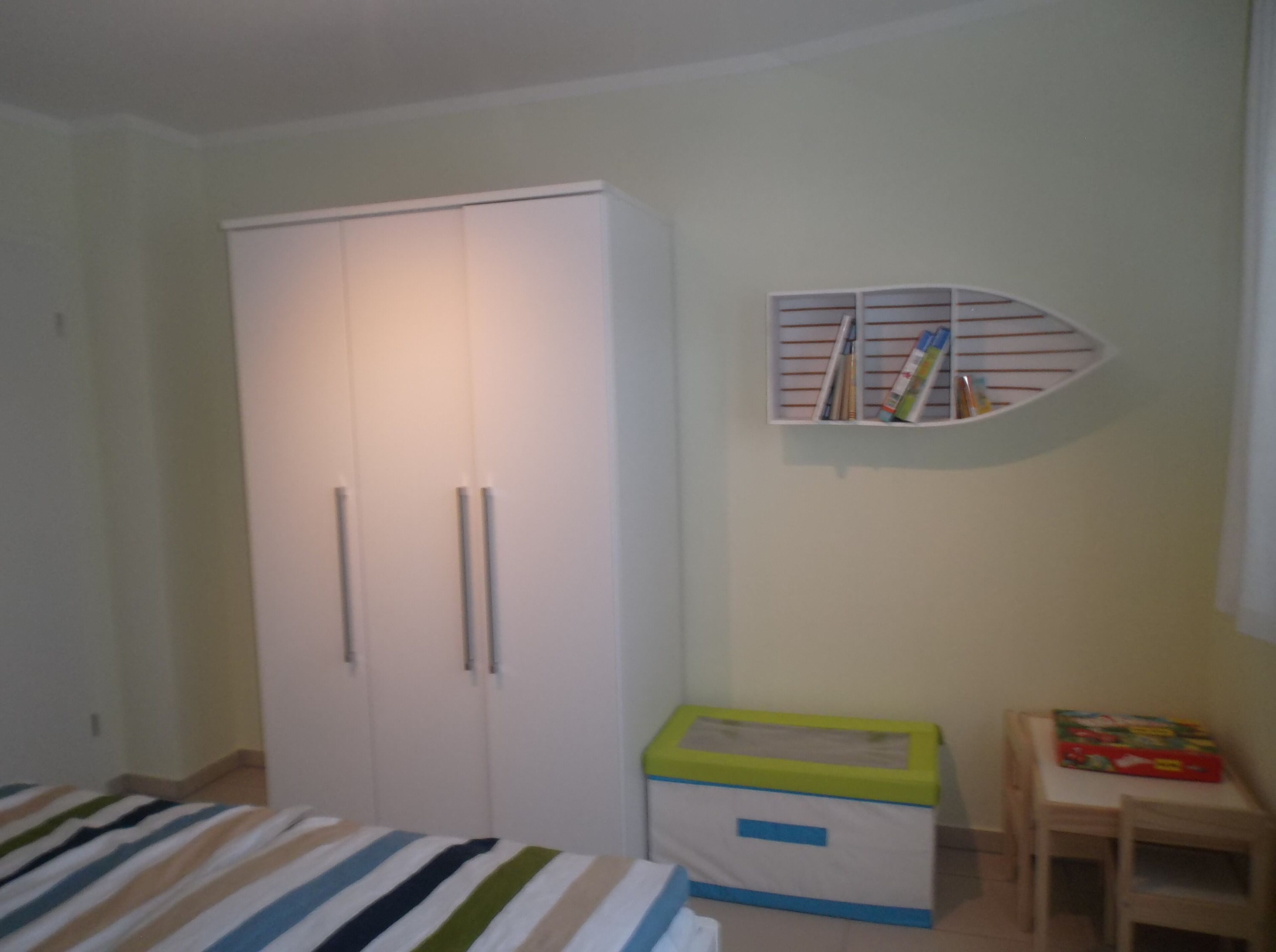 Een slaapkamer met een bed, een kledingkast, een klein bureau en een opbergdoos.