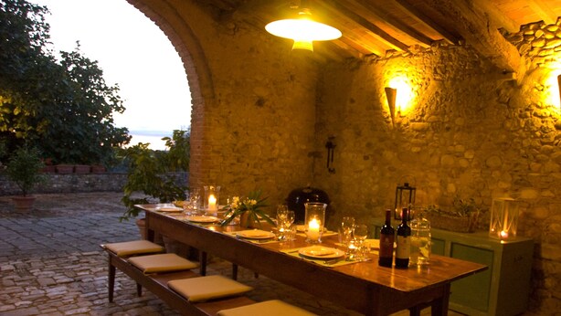 Una larga mesa de comedor preparada para una comida en una habitación de paredes de piedra con vistas al exterior.