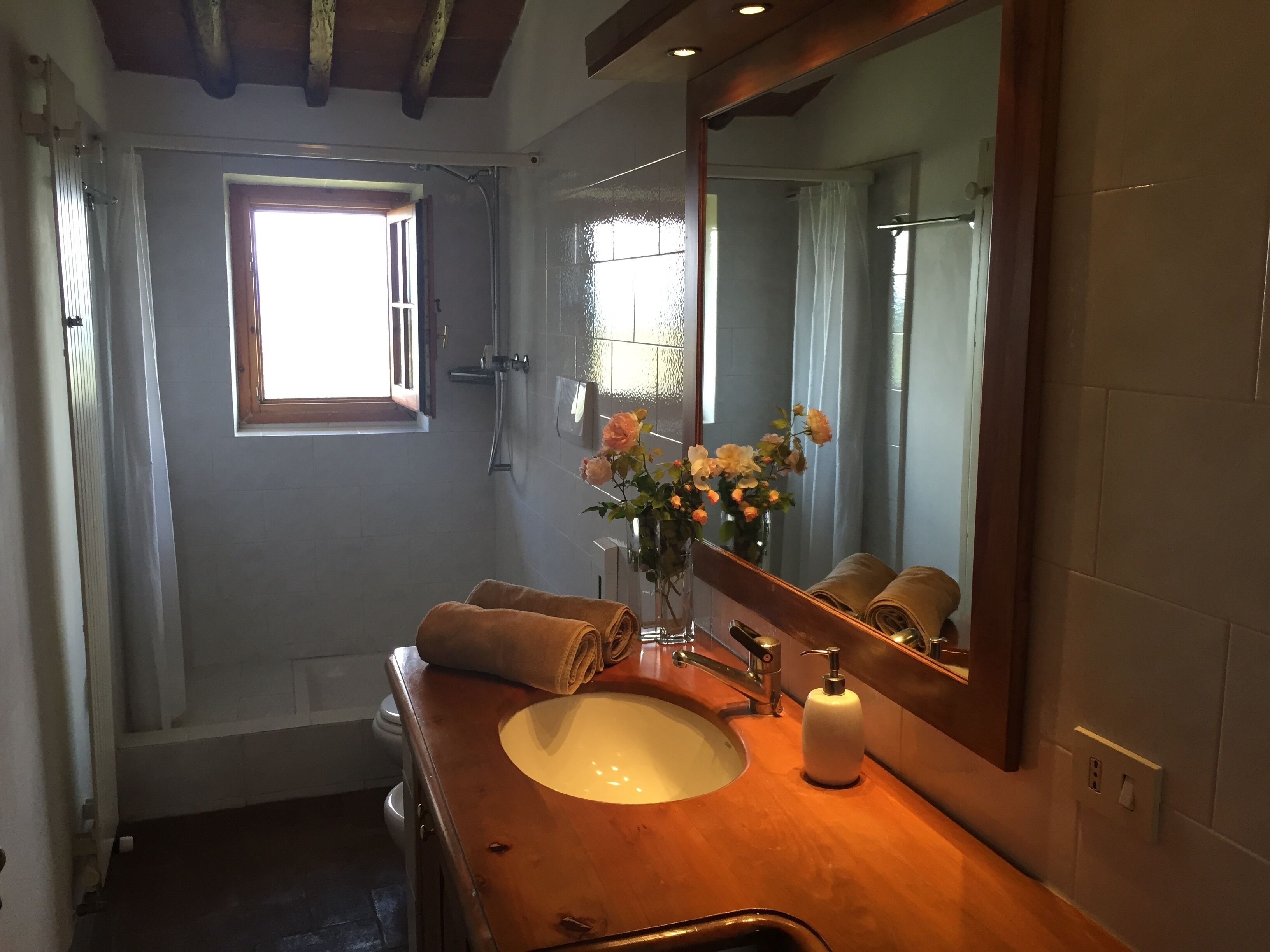 A bathroom with a wooden vanity, a white sink, a large mirror, and a window with curtains.