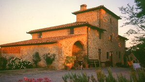 Un edificio de piedra con tejado de tejas, una entrada en arco y un pequeño jardín con macetas y flores.