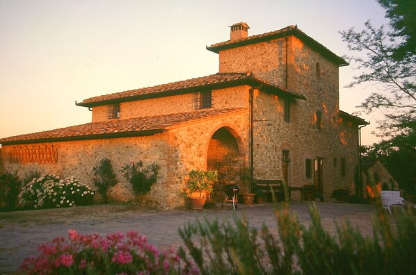 A stone building with a tiled roof, an arched entrance, and a small garden area with potted plants and flowers.