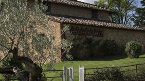 Un edificio de piedra con tejado de tejas, una valla de madera y un árbol en primer plano.