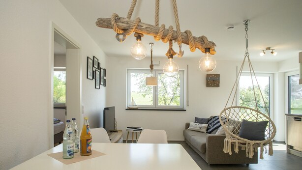 A modern living room with a white table, a hanging macramé chair, and a sofa with cushions.
