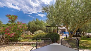 Une terrasse avec une table et des chaises, un mur en pierre et un espace piscine avec des chaises longues.