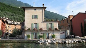 Un bâtiment à deux étages doté d’un balcon, d’un mur de pierre à l’avant et d’une montagne en arrière-plan.