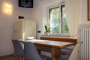 A dining area with a table, chairs, a bowl, a refrigerator, a window with curtains, and a plant. - Renovated rustic house directly on the lake. CIR:023045-LOC-00204  (Malcesine)