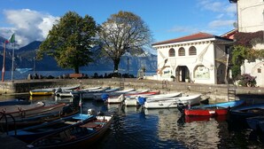 Une scène au bord de l’eau, avec des bateaux amarrés, un bâtiment doté de fenêtres en arc de cercle et un mât sur lequel flotte un drapeau.