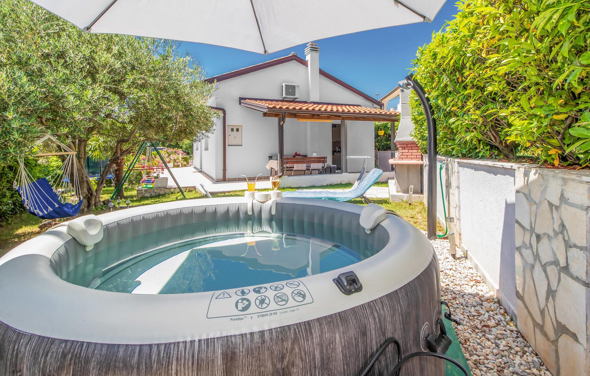 A hot tub with a control panel, a patio with a table and chairs, and a house in the background.
