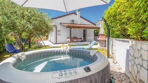 Ein Whirlpool mit Bedienfeld, eine Terrasse mit Tisch und Stühlen und ein Haus im Hintergrund.