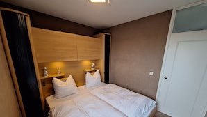 A bedroom with a bed, wooden headboard, bedside tables, and a door.