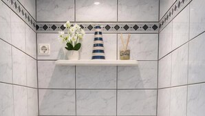 A small bathroom with a toilet, a shelf with toiletries, and a basket with toilet paper.