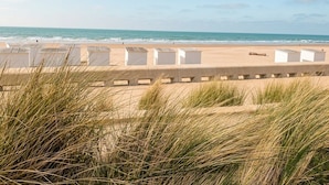 A beach with white beach huts, sand dunes, and the ocean.