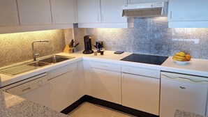 A modern kitchen with a built-in dishwasher, a coffee maker, and a fruit bowl on the counter.