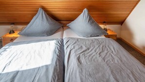 Une chambre avec deux lits, une tête de lit en bois, deux tables de chevet avec des lampes et un plafond en bois.