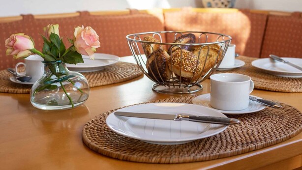 Une table à manger dressée avec des assiettes, un saladier rempli de viennoiseries, un vase de fleurs et une tasse.