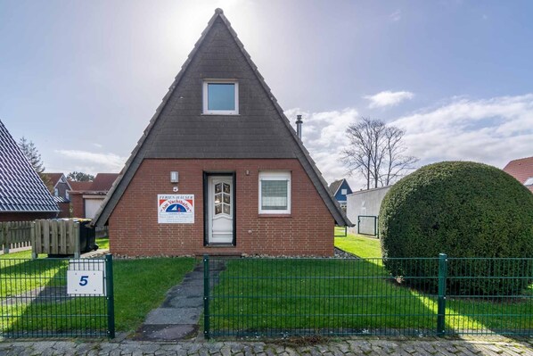 A small, triangular-roofed building with a brick facade, a small window, and a door. There is a sign on the building and a number '5' on a signboard in front.