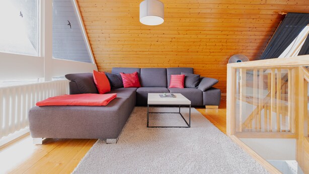 A modern living room with a grey sectional sofa, a small coffee table, and a wooden ceiling. - Light-flooded architect house in a quiet location FeWo "Red" (Edertal)