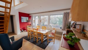 A modern living room with a dining area, wooden furniture, a black rug, and a view through large windows. - Light-flooded architect house in a quiet location FeWo "Red" (Edertal)