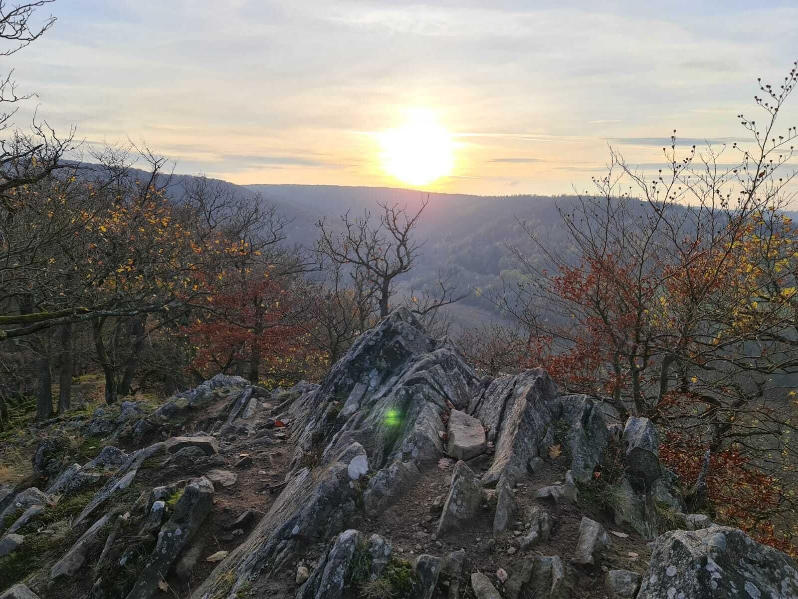 Een rotsachtig landschap met uitzicht op een ondergaande zon achter heuvels.