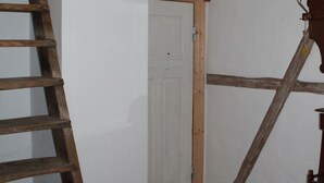 A wooden ladder leaning against a white wall, a white door, and a woven basket hanging from the ceiling.