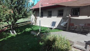A house with a red-tiled roof, a grassy yard, a hammock, a swing, and a patio with outdoor furniture.