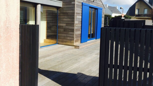 A modern house with a curved roof, a blue door, and a wooden deck. - Doëlan: Charming house facing the sea  (Clohars-Carnoët)