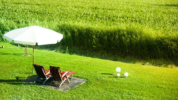 Et græsstykke med en hvid parasol, to stole og et lille bord.