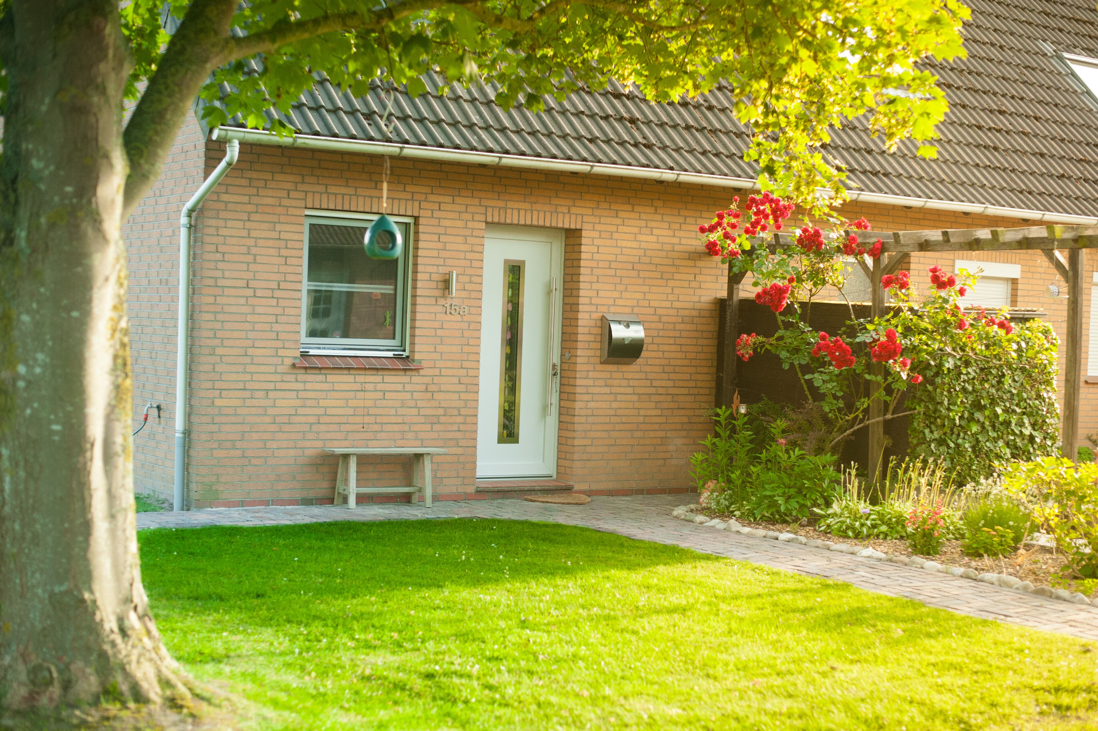 A brick house with a white door, a mailbox, and a small bench.