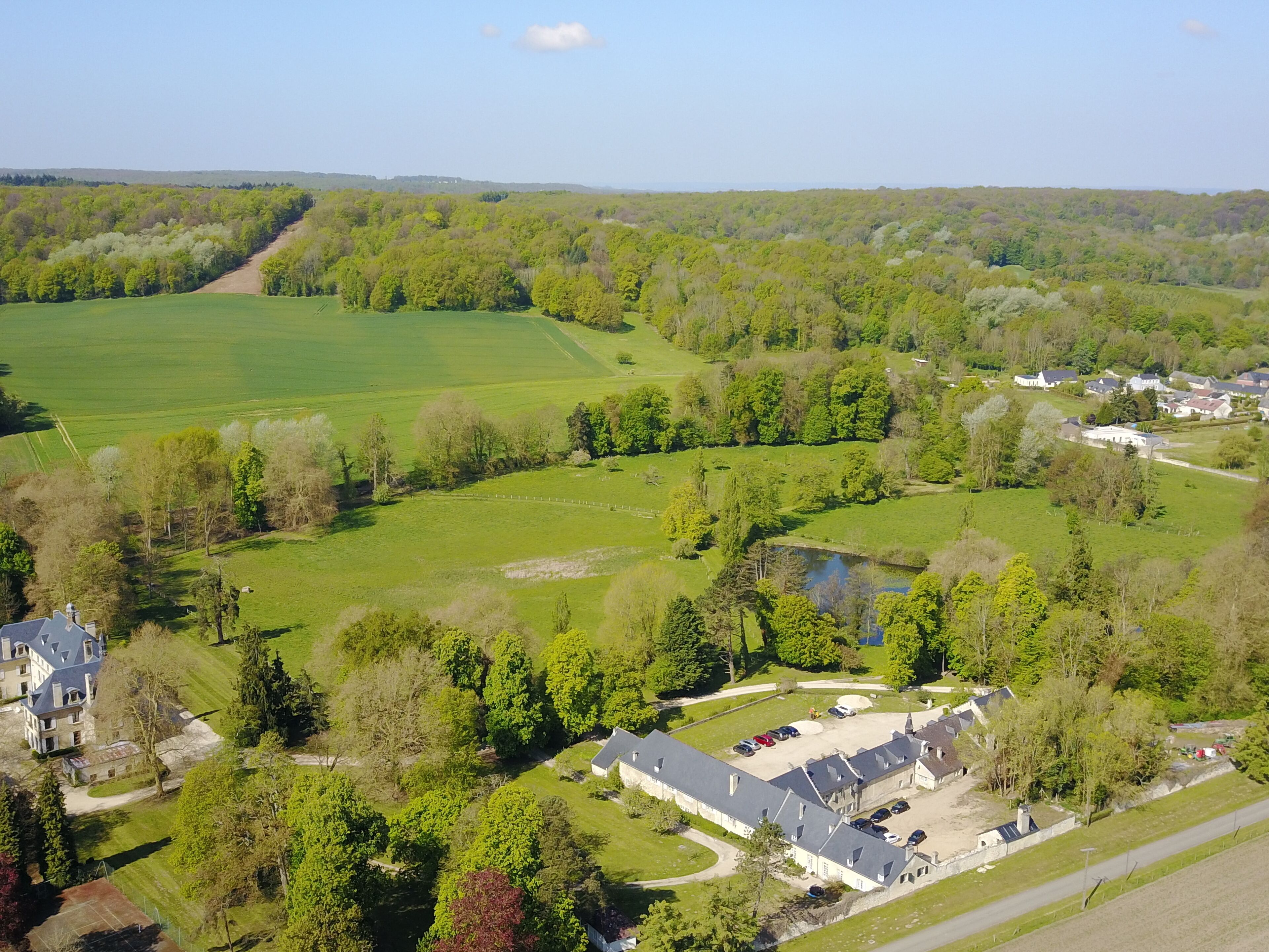 Vue aérienne d’une propriété rurale comprenant une grande maison, plusieurs bâtiments plus petits et de vastes champs verdoyants.