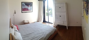 A bedroom with a bed, a nightstand, a lamp, a wardrobe, and a painting on the wall.