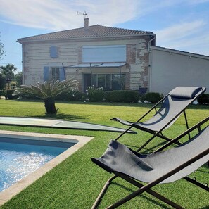 A house with a swimming pool, a garden, and two lounge chairs.