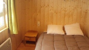 Een kamer met houten lambrisering, een bed, een klein houten nachtkastje en een raam met gordijnen.