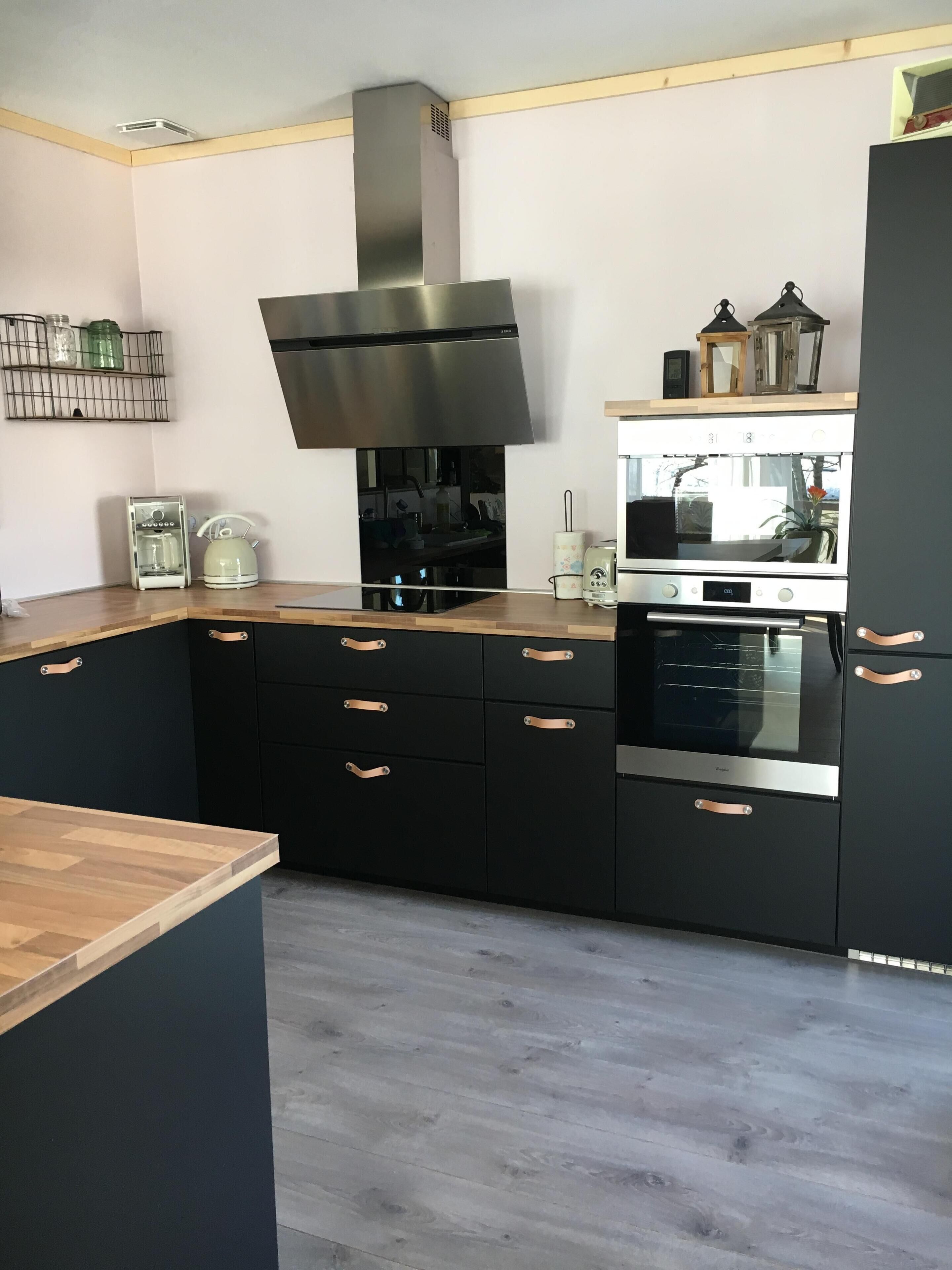 A modern kitchen with black cabinets, a stainless steel range hood, and a built-in oven.