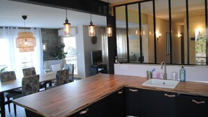 A modern kitchen with a wooden countertop, black cabinets, and a large mirror. There is a dining area with a table and chairs, and a television in the background. - Detached house 3 Bedrooms, 140 M2, Loggia, Balcony, private garden 800 M2 (Les Hôpitaux-Neufs)