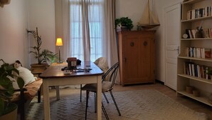 A cozy living room with a wooden table, a sofa, a bookshelf, and a window with curtains. - T2 apartment with south-facing terrace (Cotignac)