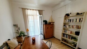 A cozy living room with a wooden table, a sofa, a bookshelf, and a window with curtains. - T2 apartment with south-facing terrace (Cotignac)