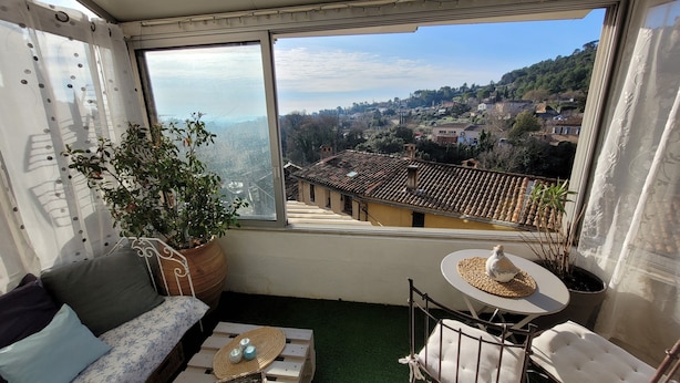 A balcony with a sofa, a small table, and a chair, overlooking a scenic village. - T2 apartment with south-facing terrace (Cotignac)