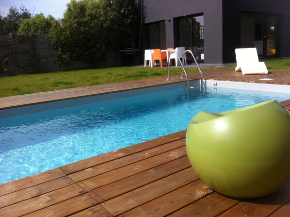 A swimming pool with a wooden deck, a green exercise ball, and outdoor seating.