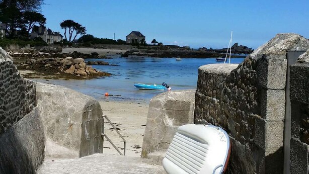 A coastal pathway leading to a beach with a white object on the ground, stone walls, and a clear blue sky.
