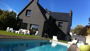 A modern house with a swimming pool, white lounge chairs, and a wooden deck.