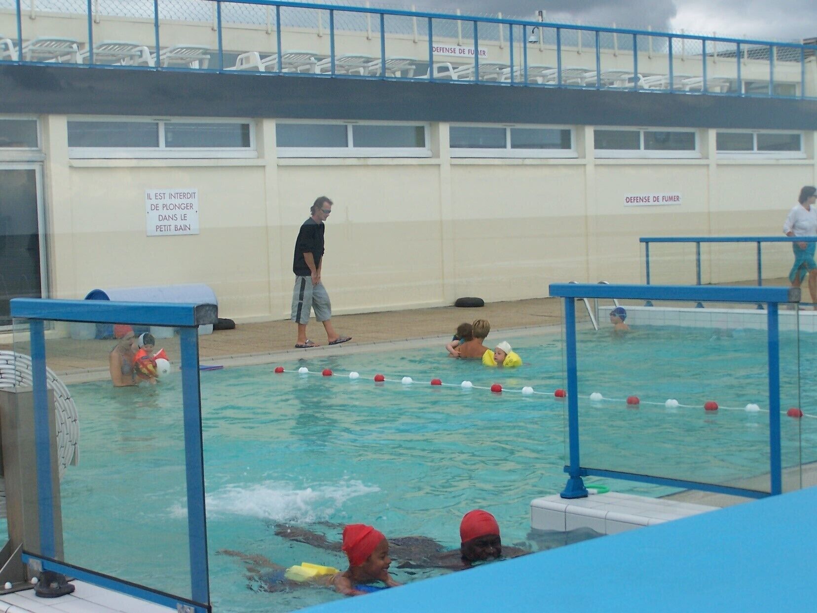 A swimming pool with a lifeguard tower, a sign indicating no diving, and a fenced area with chairs.